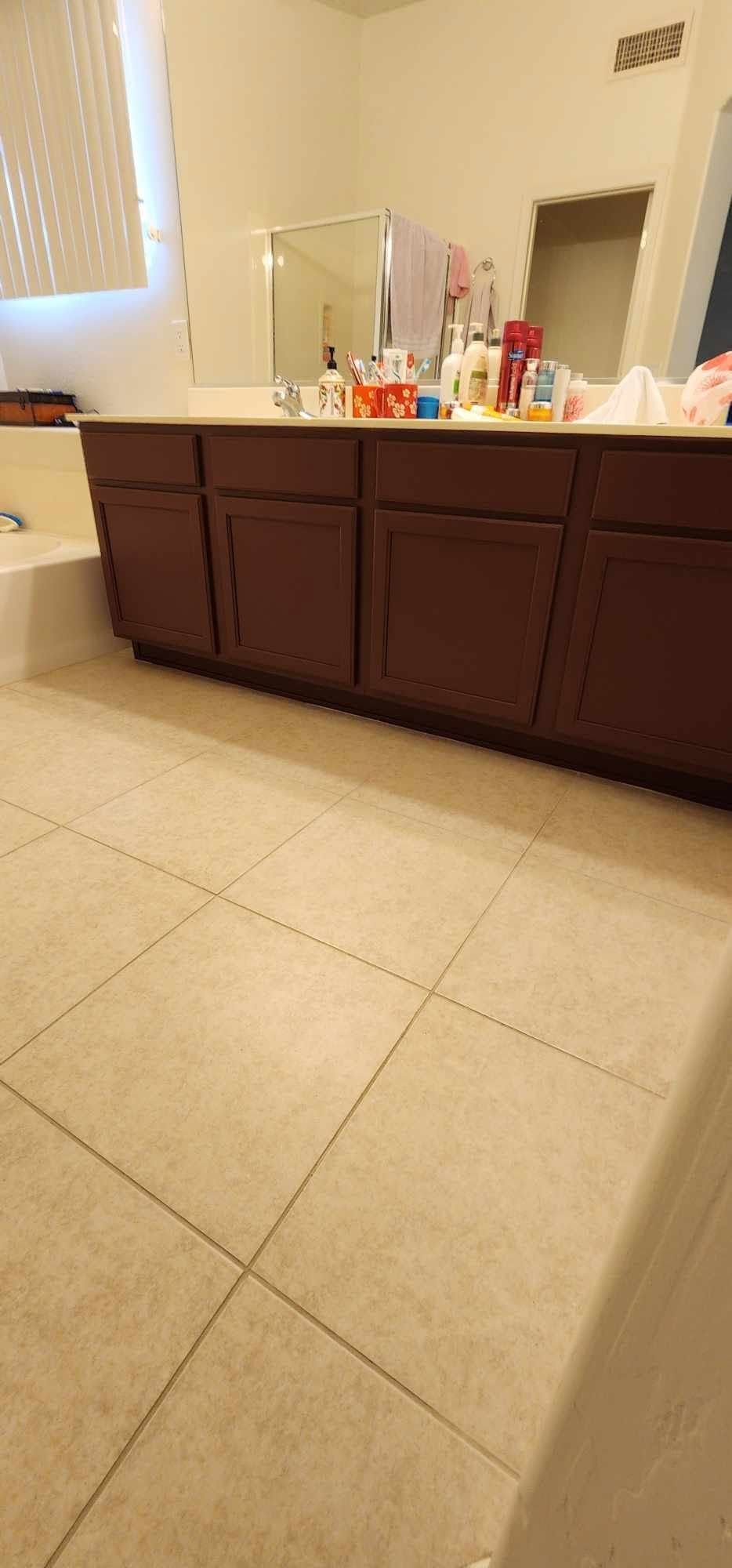 Bathroom with dark wood vanity, beige tile floor, and toiletries arranged along the countertop.
