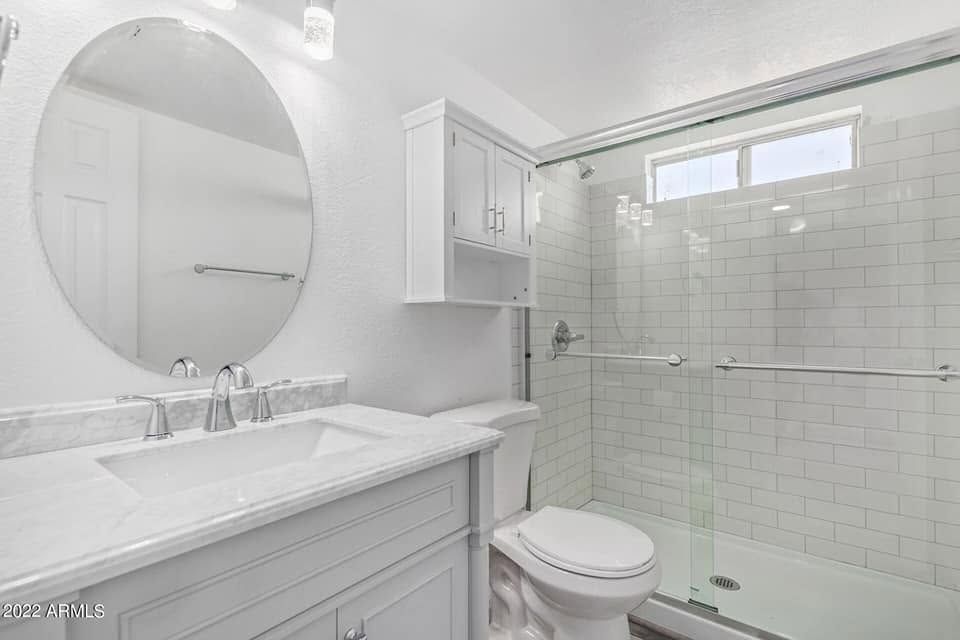 Bright white bathroom with double vanity, round mirror, and glass shower enclosure