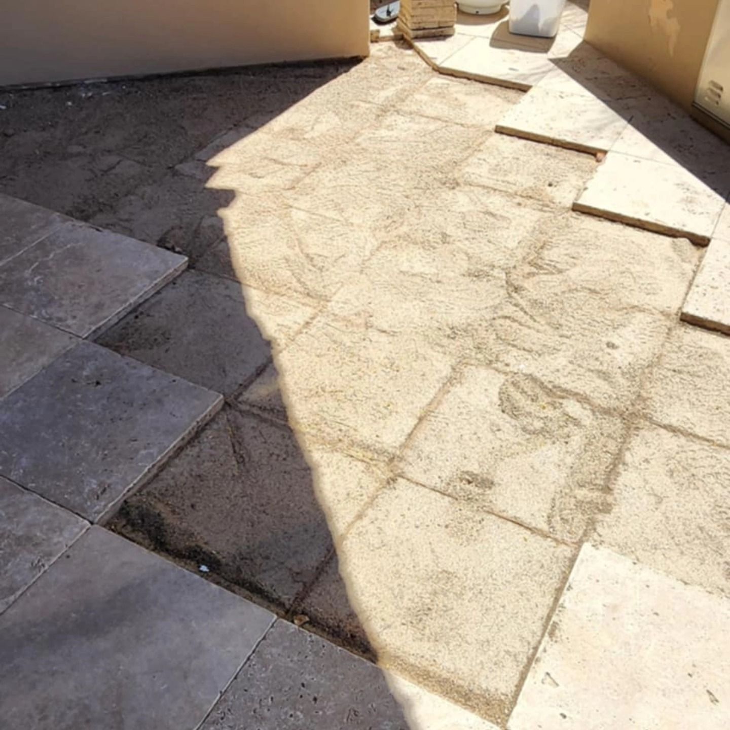 Sunlit outdoor patio with cracked paving stones and a wall casting shadows