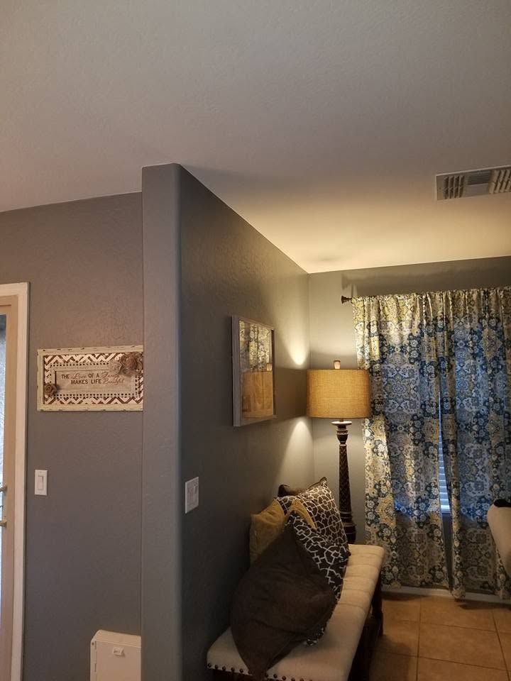 Living room corner with gray walls, a sofa, lamp, curtains, and wall art near a doorway