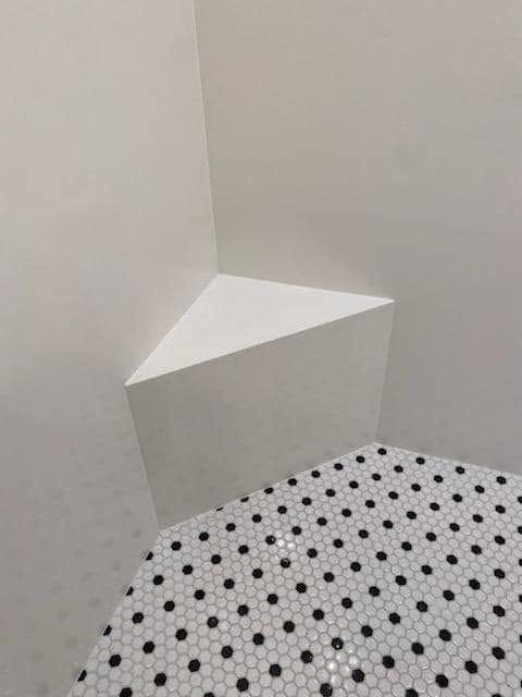 White geometric shelf in a corner above a black polka-dot surface