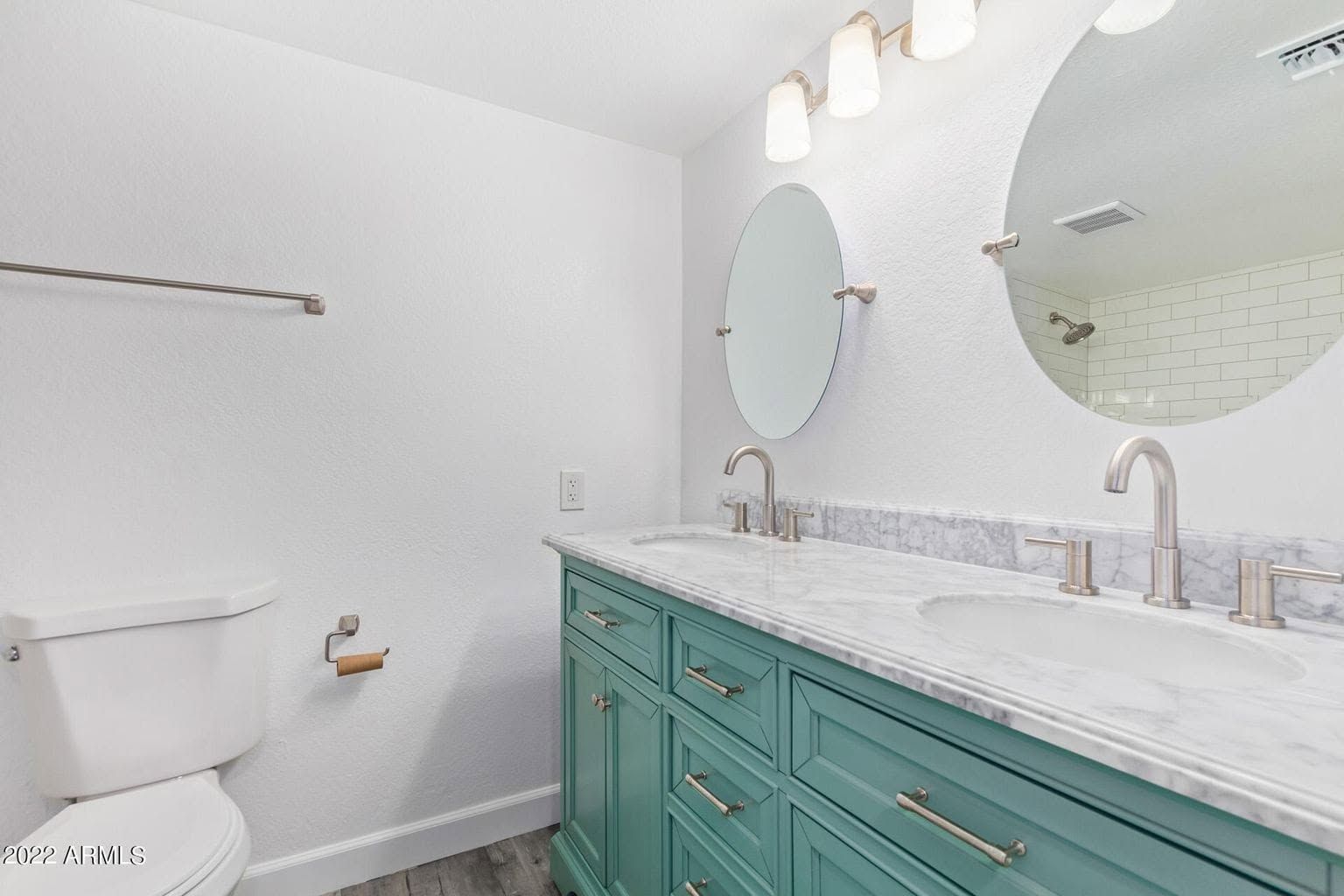 Bright bathroom with teal vanity, double sinks, round mirrors, and a toilet.