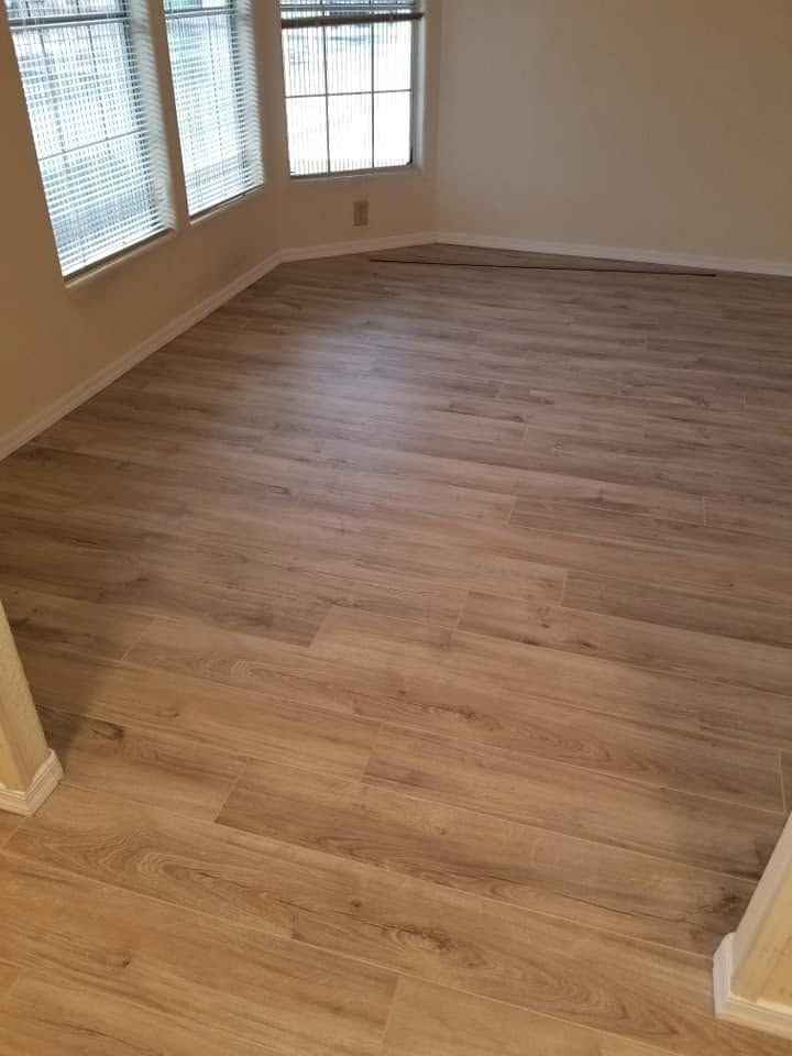 Empty room with light wood flooring and large windows with blinds.