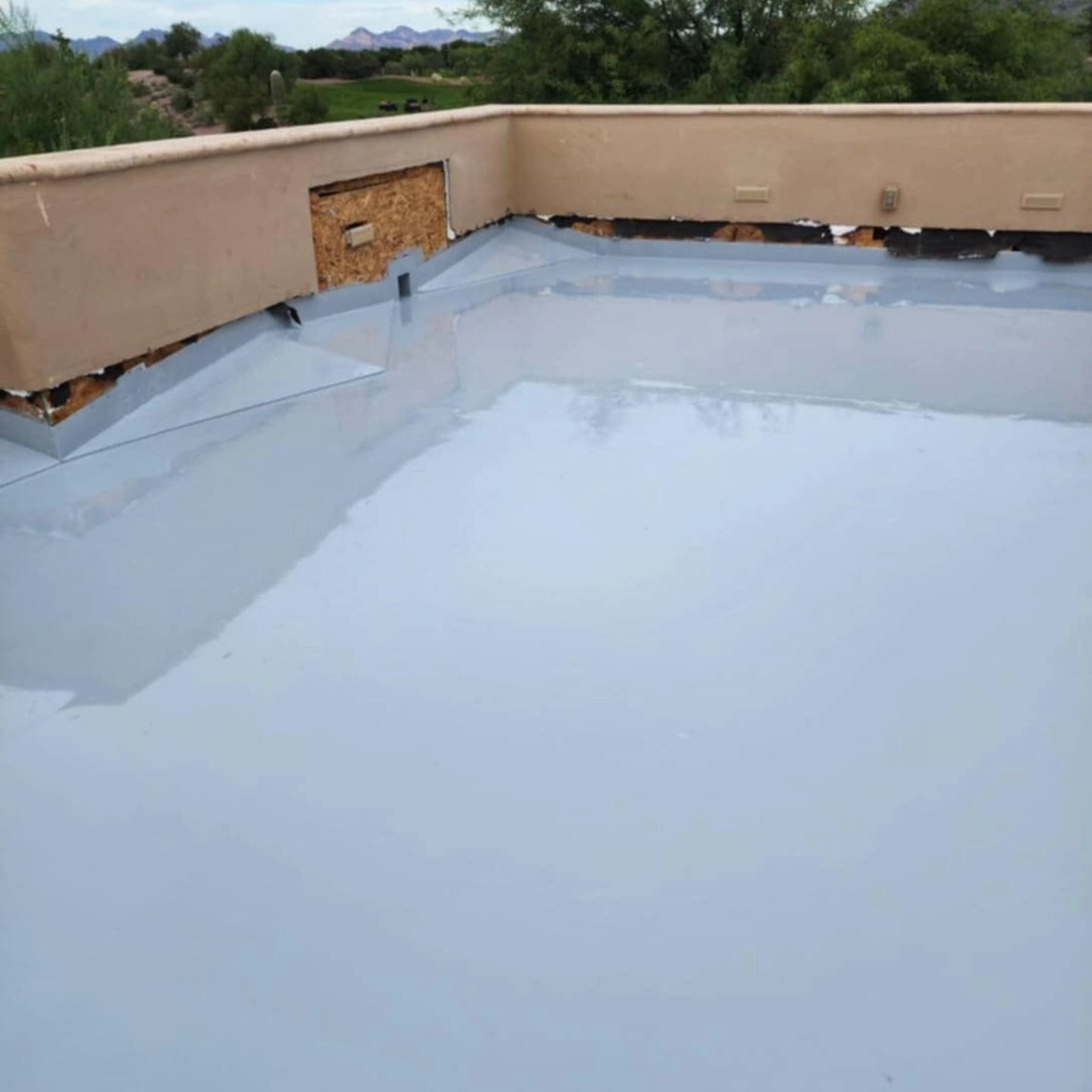 Flat white-coated rooftop with beige parapet walls and a patched corner section under open sky.