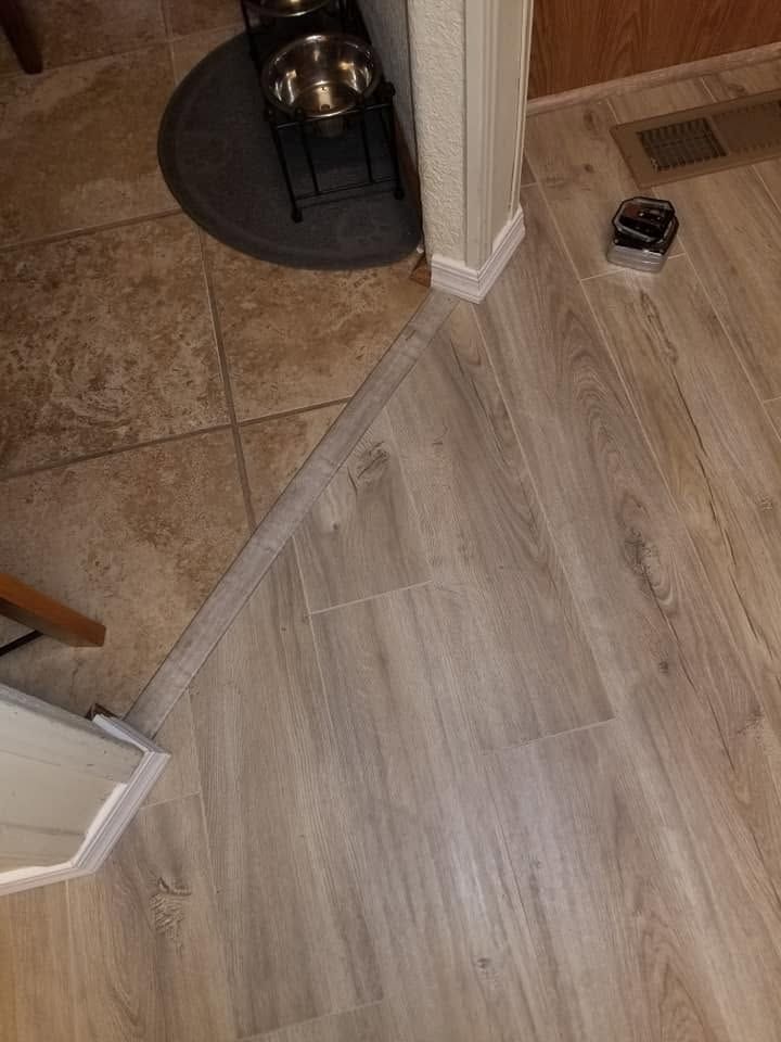 Hallway corner with beige tile and gray wood-look flooring, dog bed, and small black object on the floor.