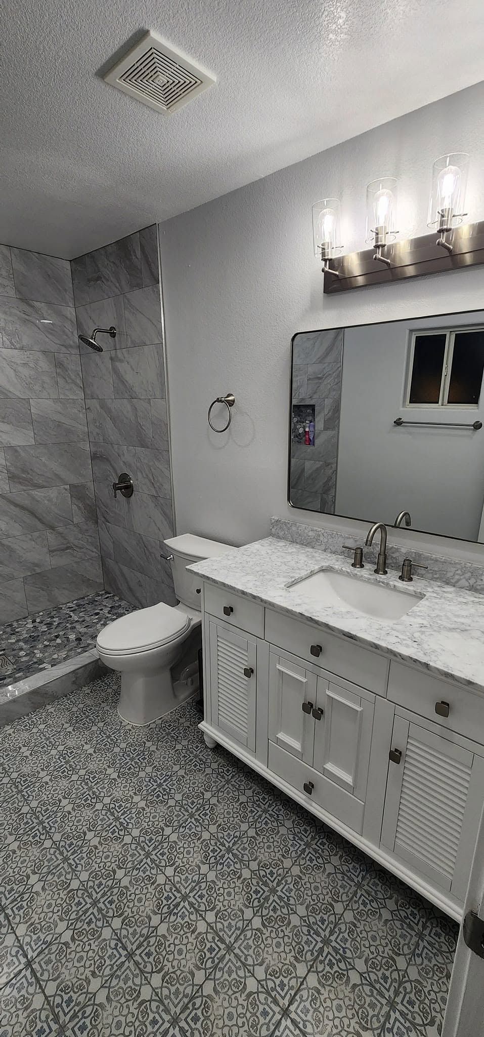 Modern gray bathroom with double vanity, large mirror, shower, and patterned tile floor.