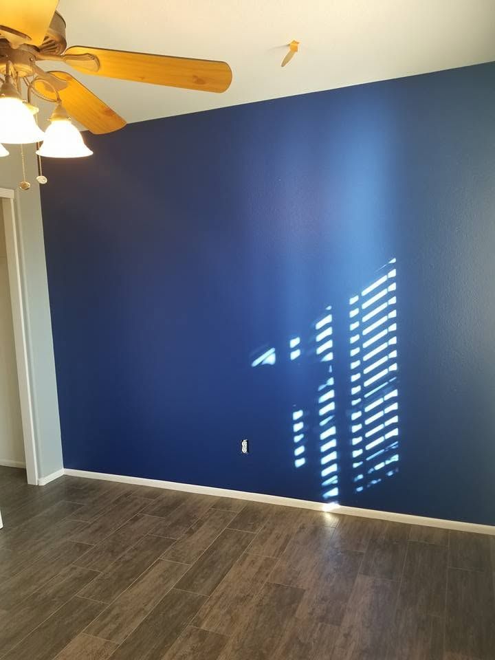 Empty room with deep blue accent wall, dark wood floor, and sunlight through blinds casting stripes.