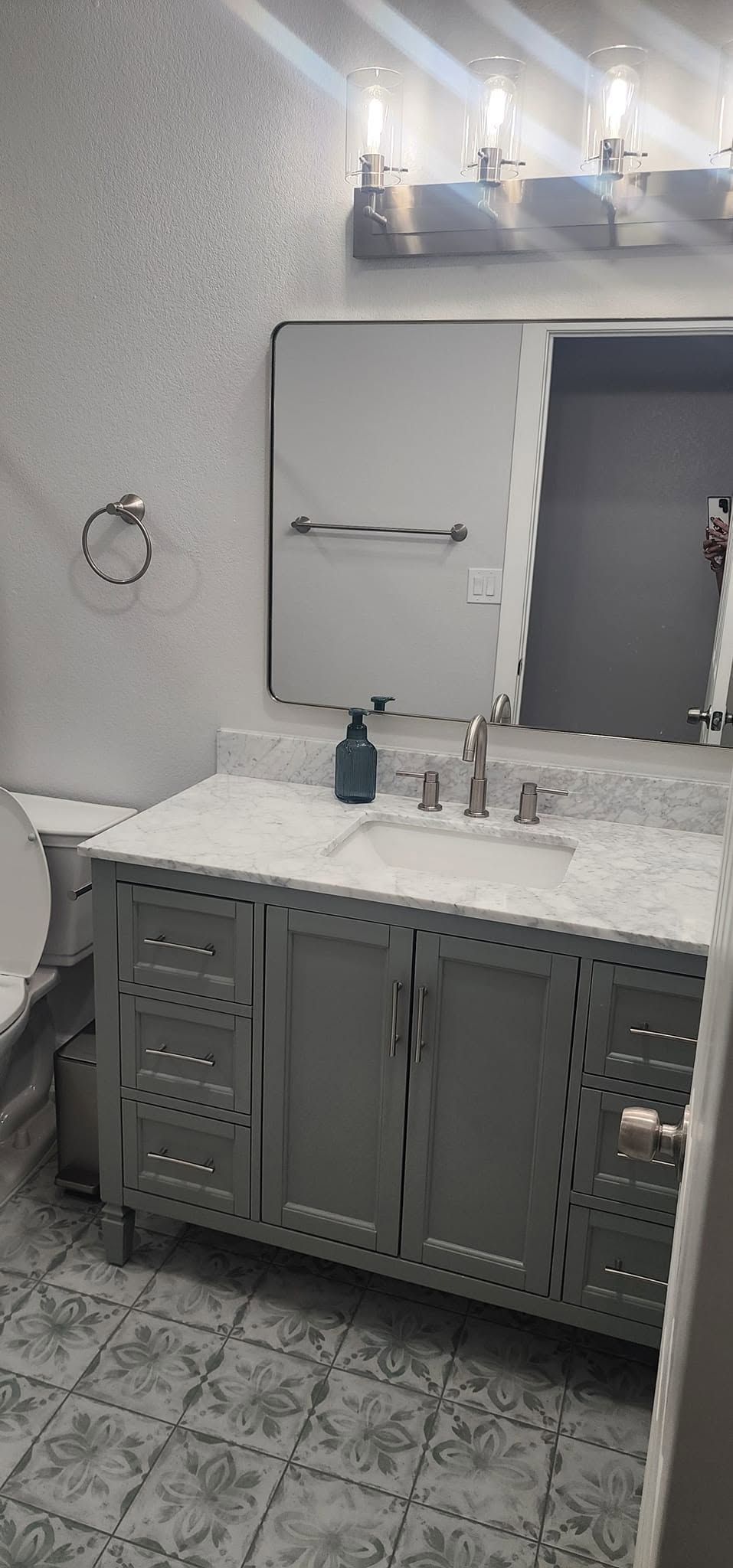 Modern bathroom with gray vanity, wall mirror, sink, tiled floor, and wall lights