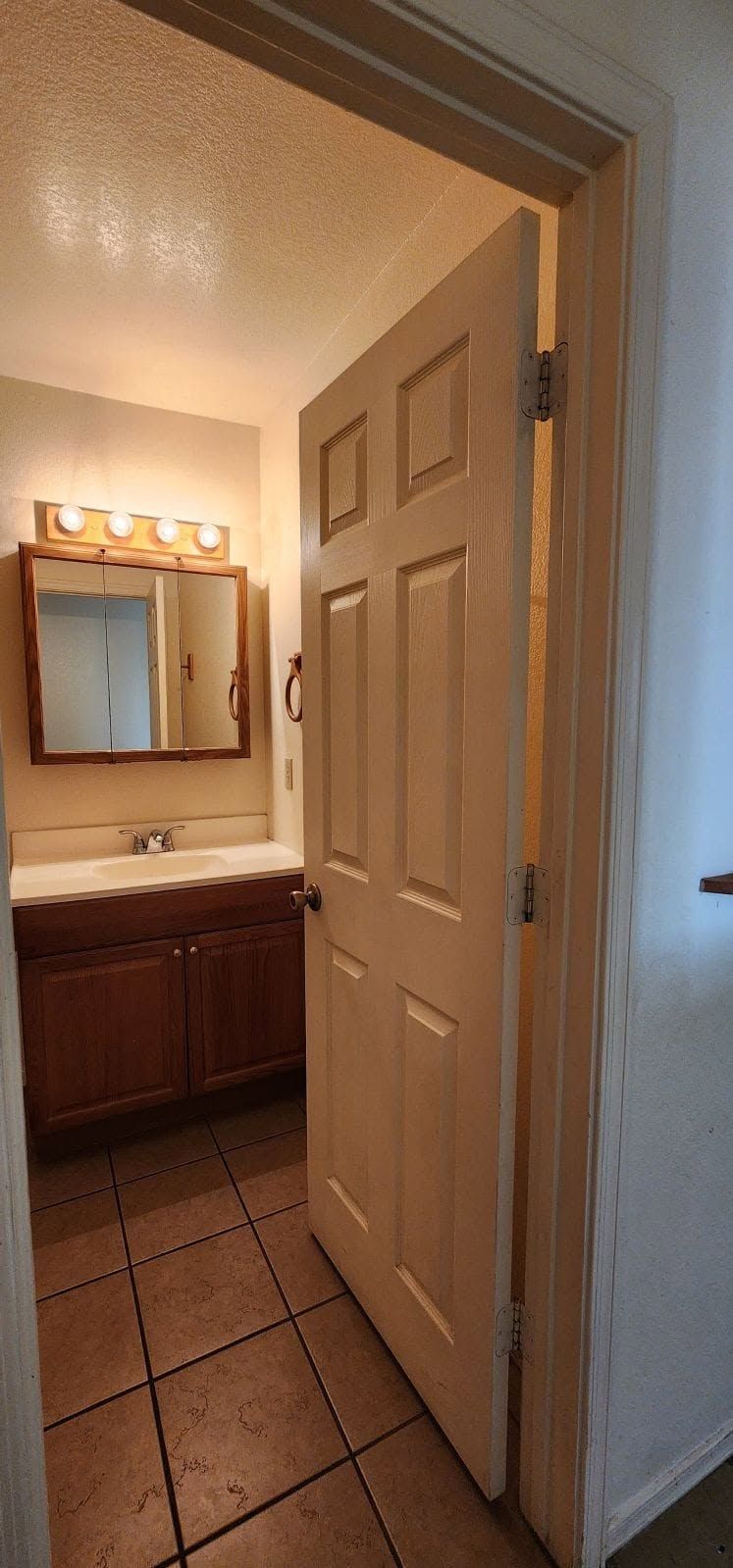 Open bathroom door revealing a vanity, mirror, and warm-lit tiled floor.
