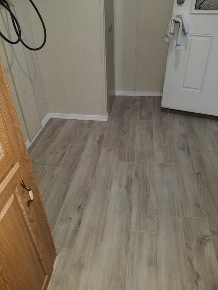 Small hallway with gray wood flooring, beige walls, a white front door, and a wooden cabinet edge.