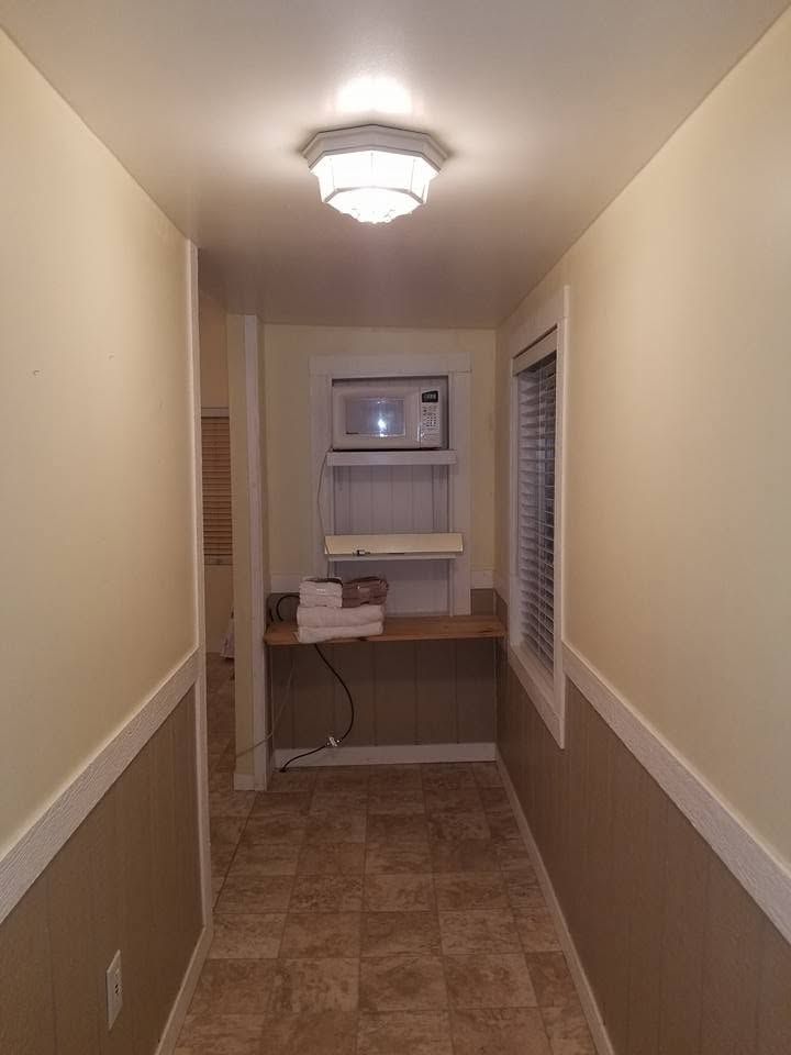 Narrow hallway with beige walls, tiled floor, and a small desk beneath a window at the end.
