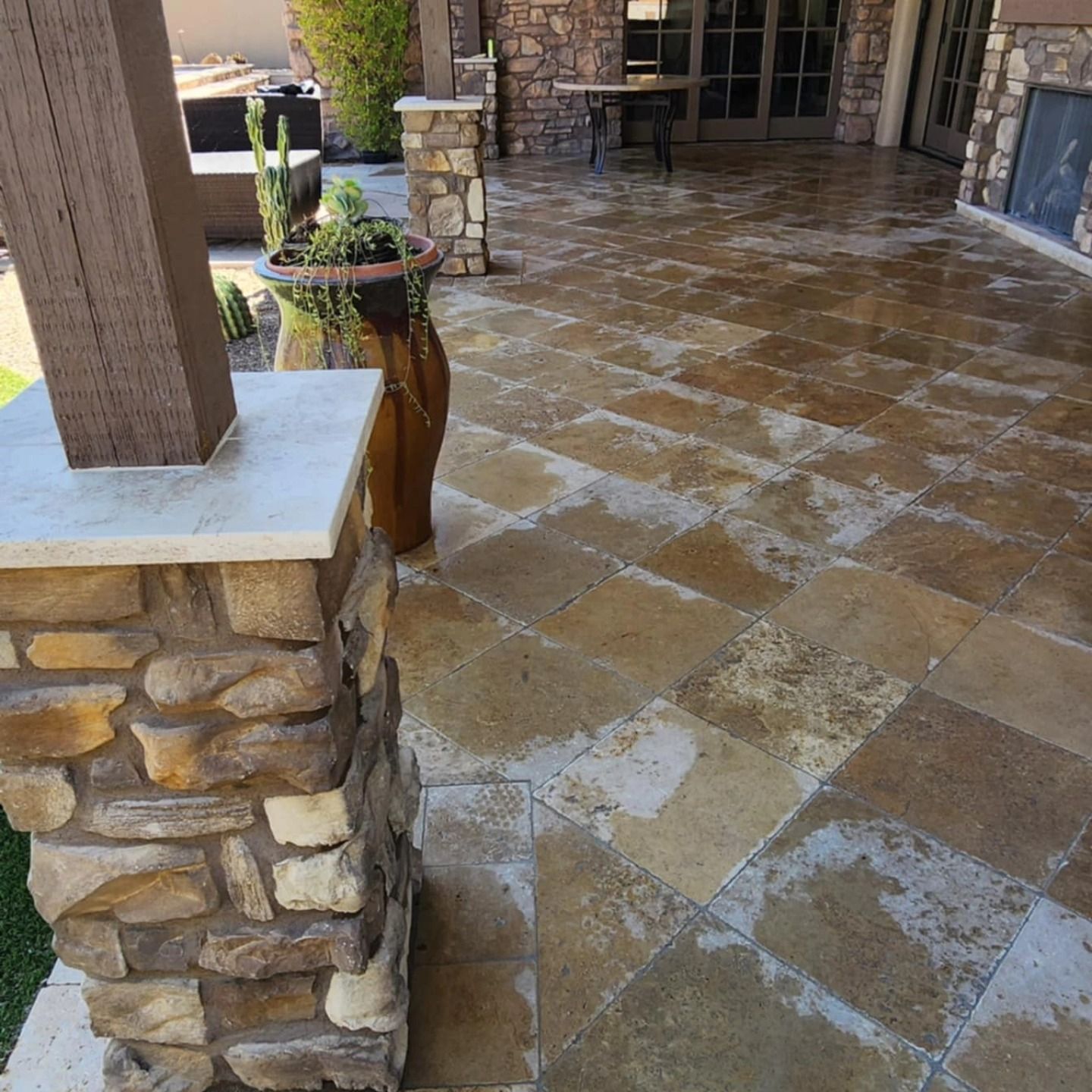 Stone-tiled covered patio with columns, planters, and wet floor