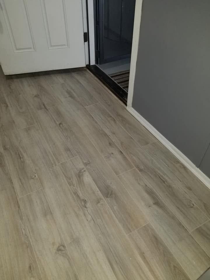 Light wood flooring in a hallway beside a white door and gray wall
