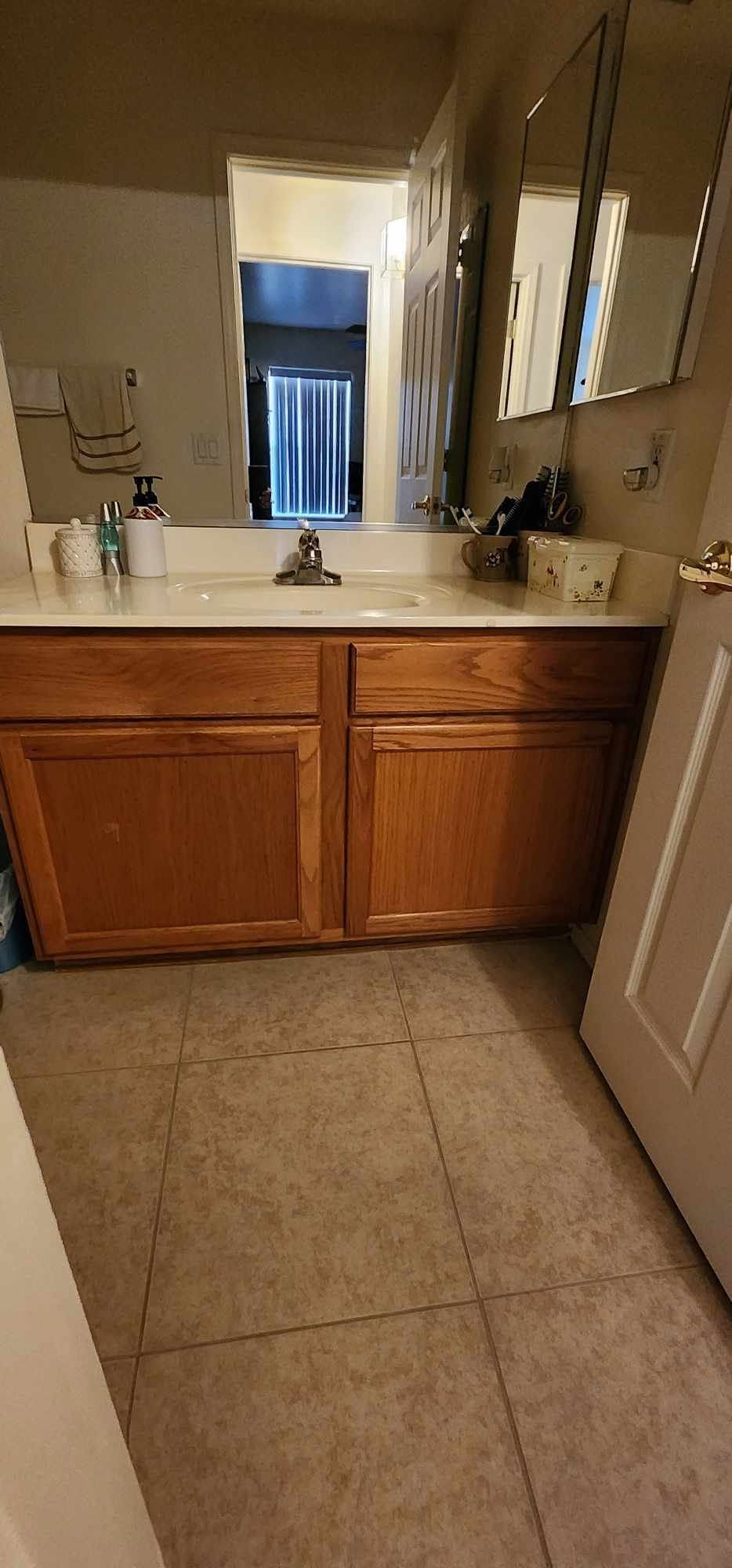 Small bathroom vanity with wood cabinets, beige countertop, mirror, and tiled floor.