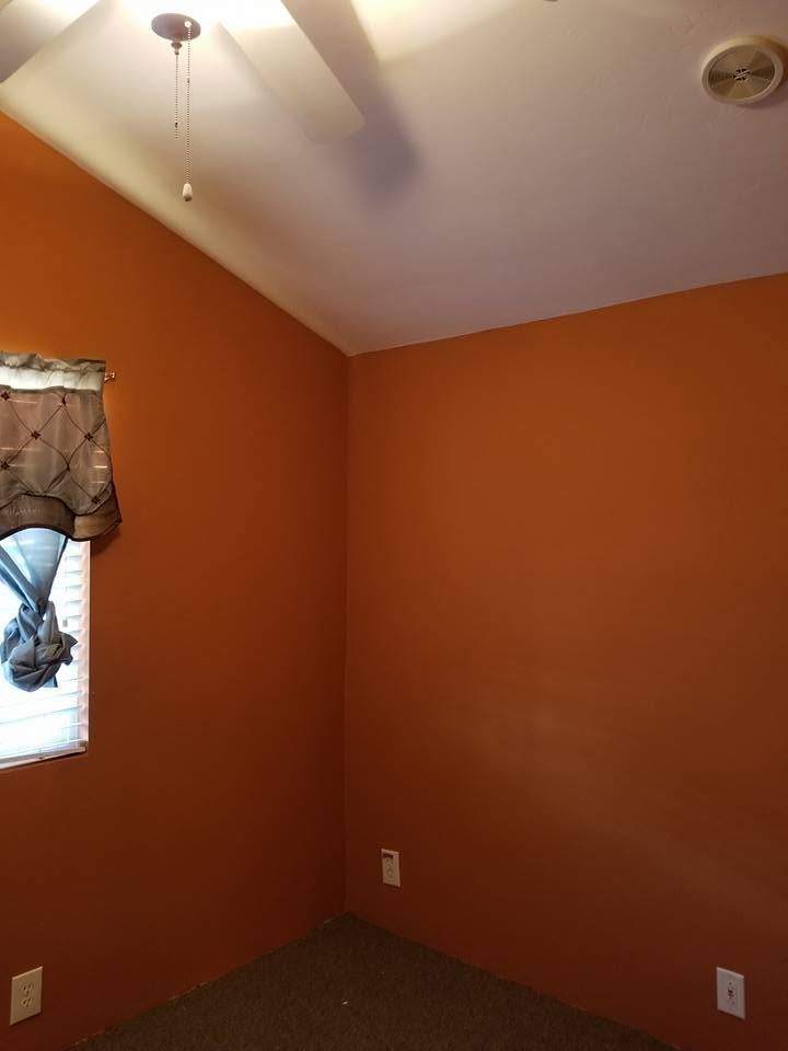 Empty orange bedroom corner with white ceiling, window, and ceiling fan.
