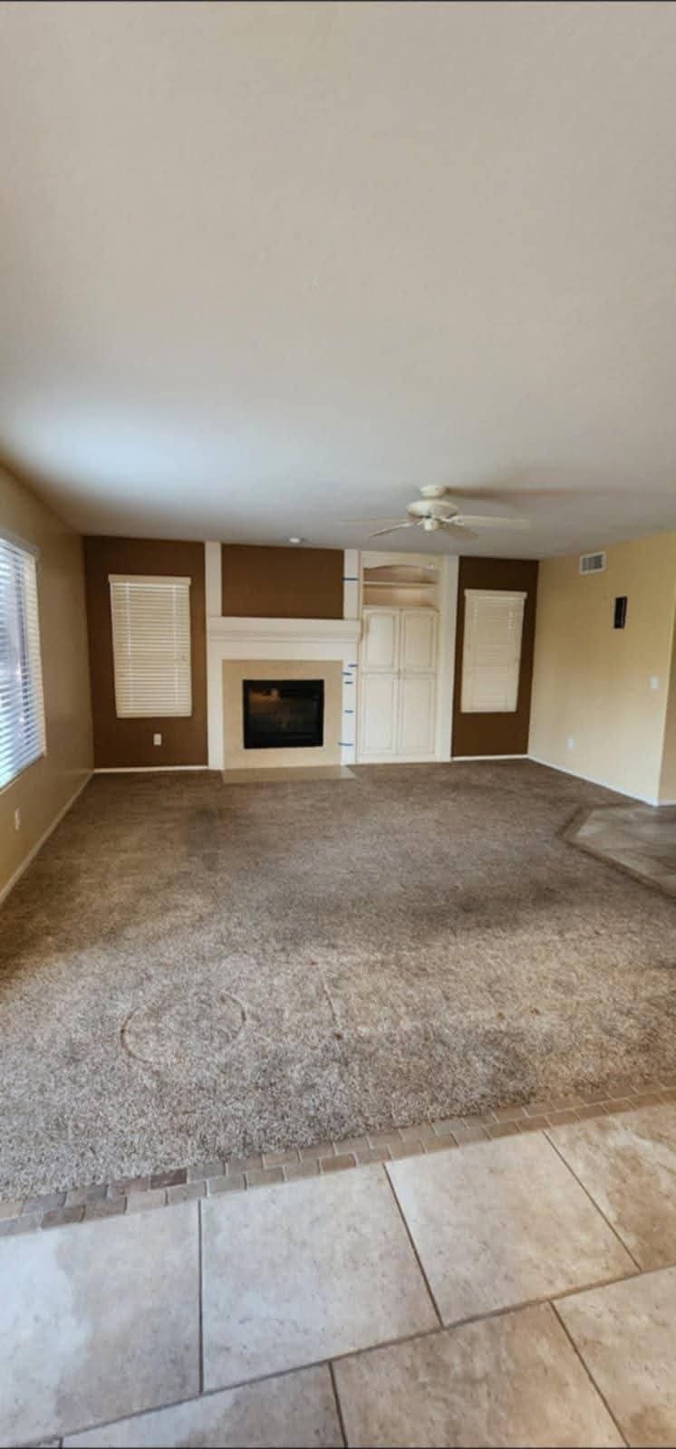 Empty living room with beige carpet, tiled floor, fireplace, and window shutters