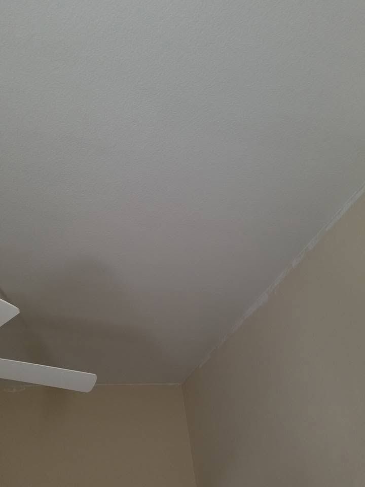 Beige room corner with white ceiling and partial white ceiling fan blade.