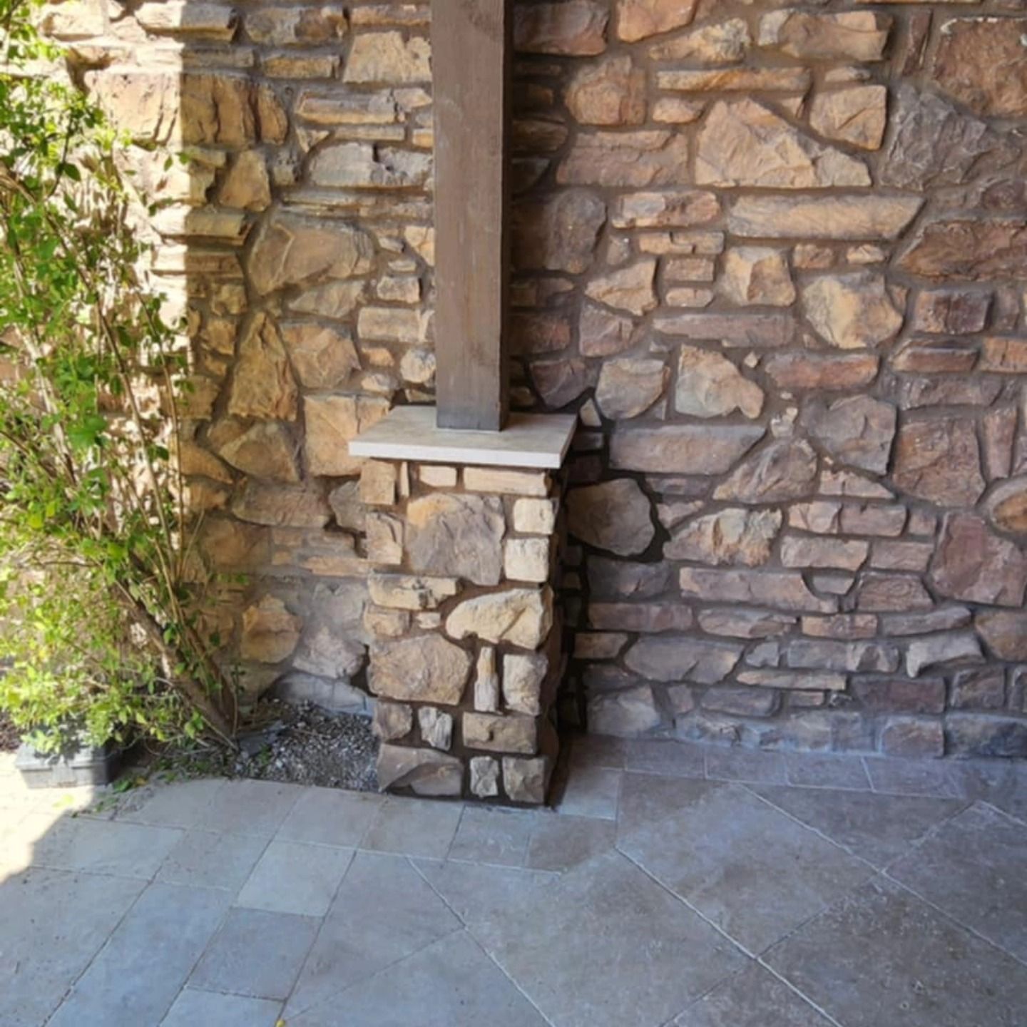 Stone patio corner with textured wall and a narrow vertical column beside a planter.