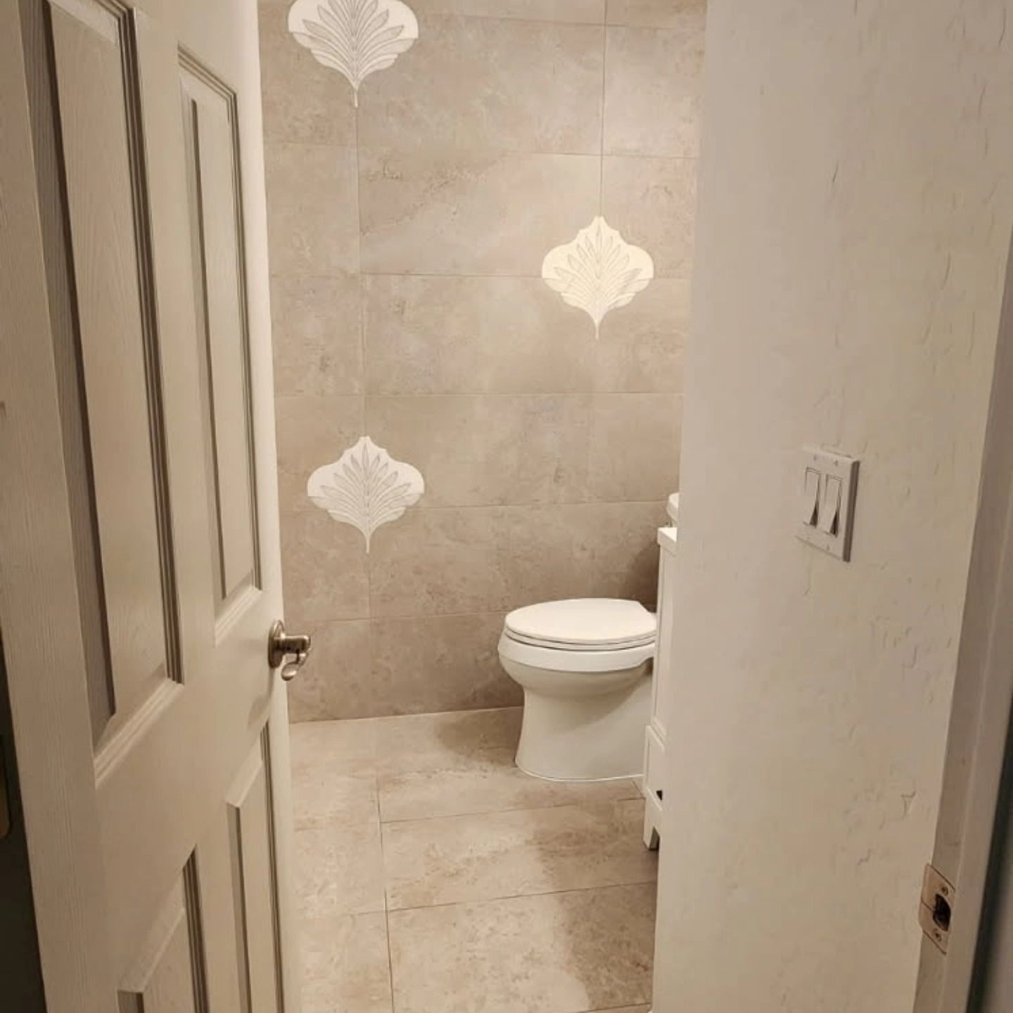 Small beige-tiled bathroom with a toilet and a partially open door.