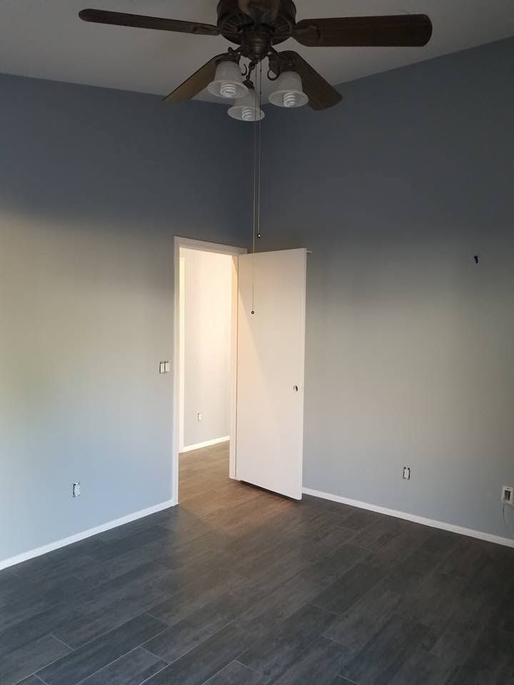 Empty room with gray walls, dark wood floor, ceiling fan, and open door to a bright hallway.