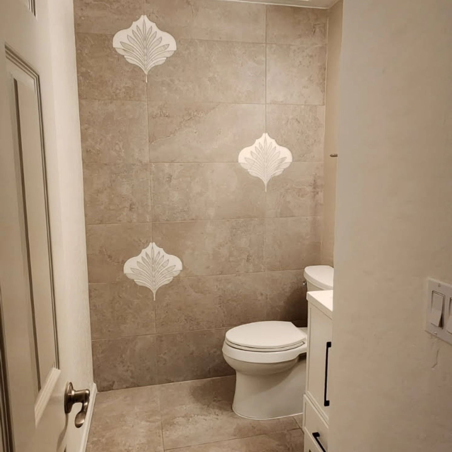 Small beige bathroom with decorative tile wall and a toilet beside a sink vanity