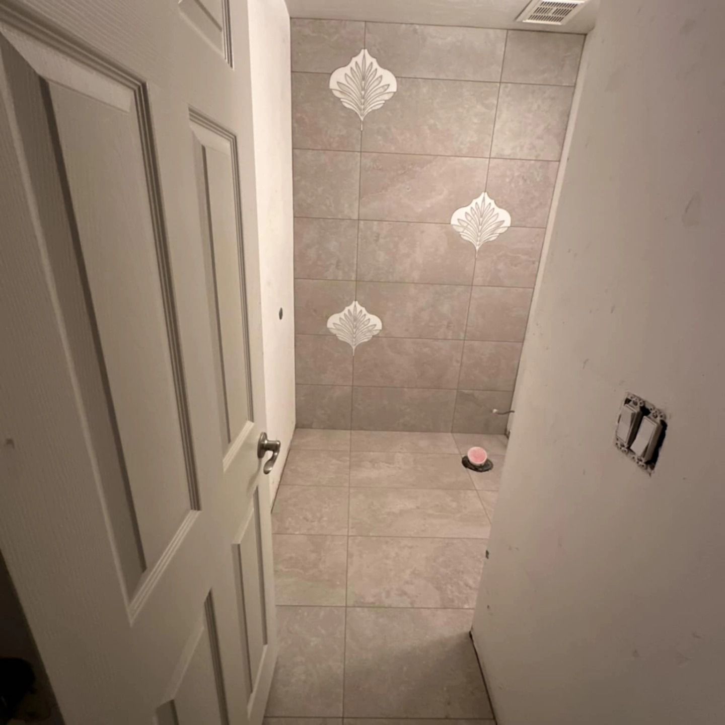 Small unfinished bathroom with gray tiled shower wall and a single pink drain cover on the floor.