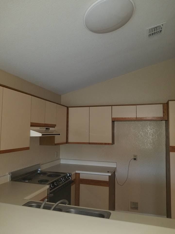 Small beige kitchen with cabinets, stove, sink, countertop, and refrigerator under a ceiling light.