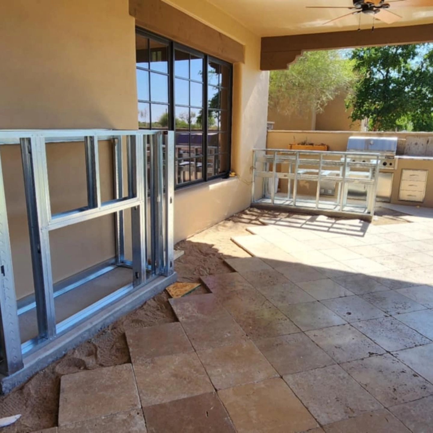 Covered patio with stacked aluminum frames, a window, and a countertop workspace on a tiled floor.
