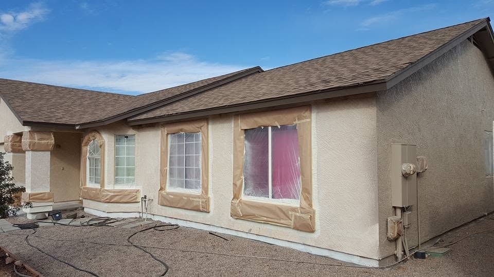 Single-story beige stucco house with brown roof and multiple front windows under a clear blue sky
