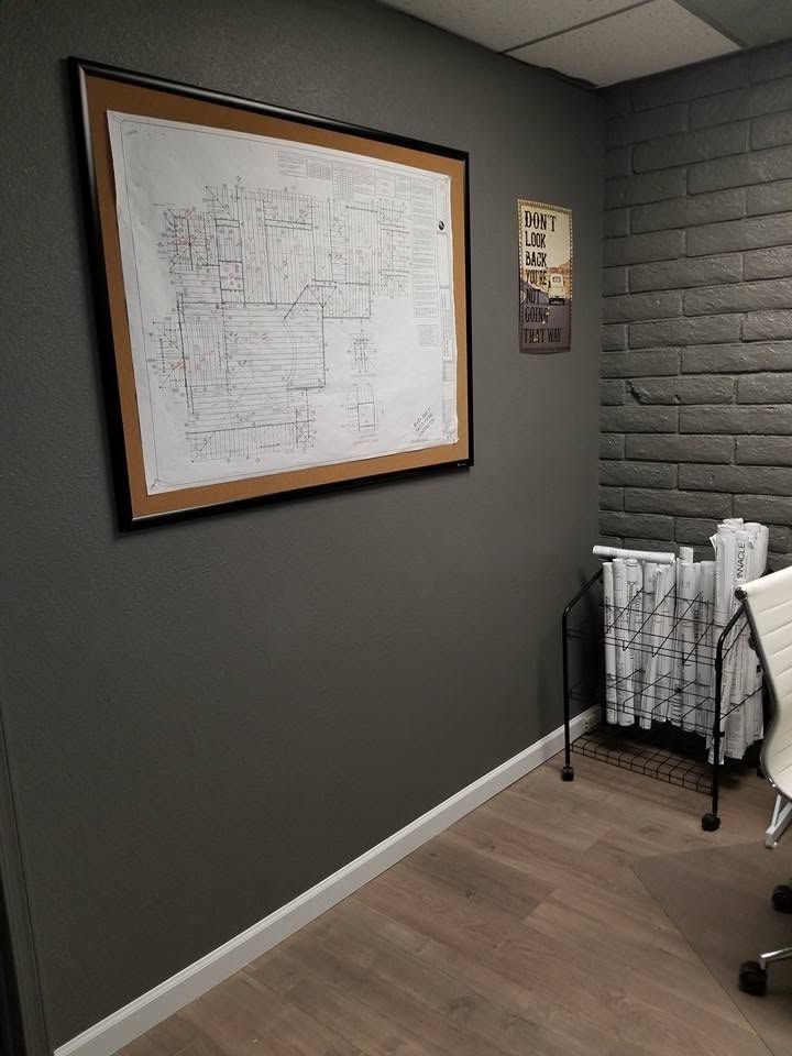 Framed floor plan on a gray office wall beside a brick accent wall and folded rack of linens.