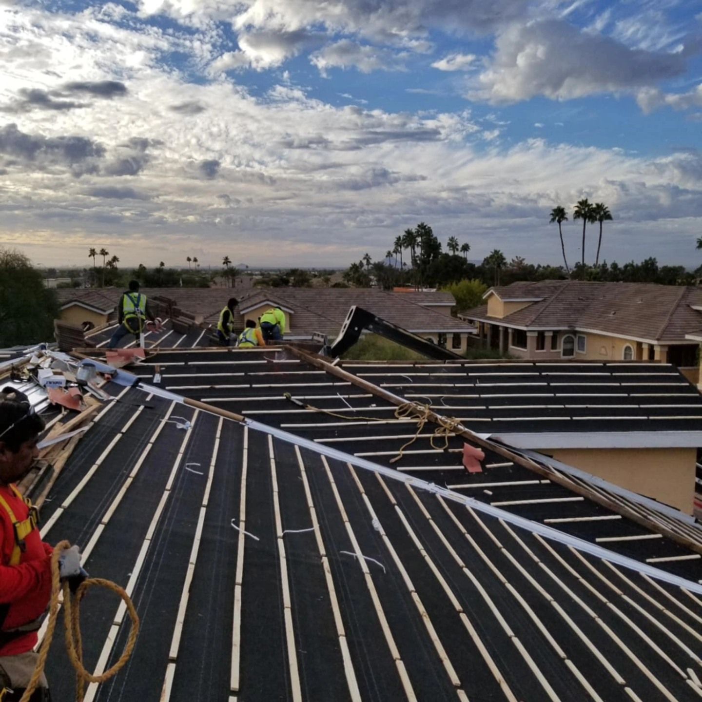 Roofers installing panels on a house roof under a cloudy sky, with workers and tools visible.