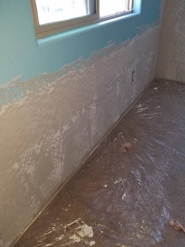 Partially painted room with a window, scuffed lower wall, and a bare floor with debris and dust