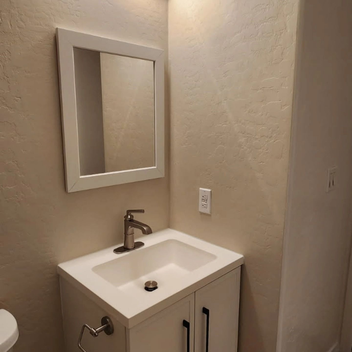 Small beige bathroom vanity with sink, mirror, and wall outlet beside a shower stall