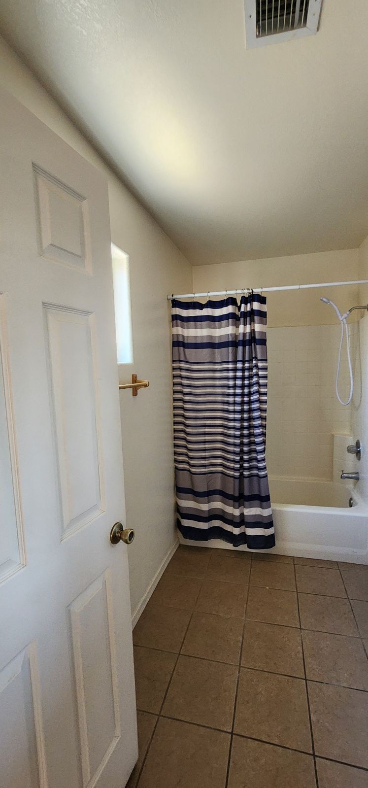 Small bathroom with white door, striped shower curtain, beige tile floor, and a bathtub.