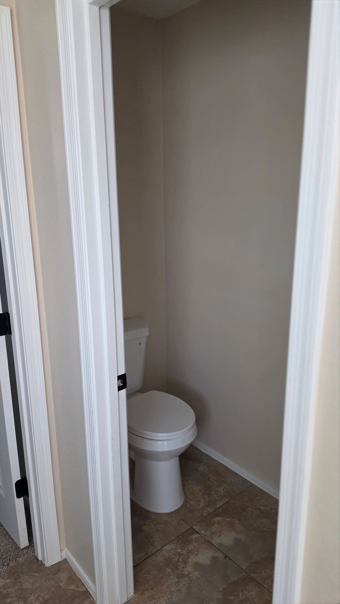 Small bathroom with an open door, showing a white toilet and beige tile floor.