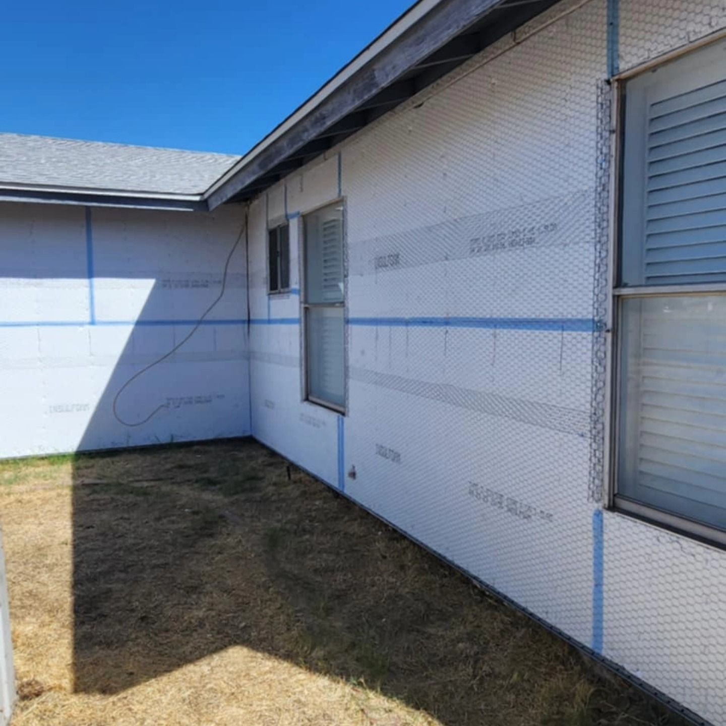 Exterior of a white building with blue trim, windows, and a small side yard under clear sky