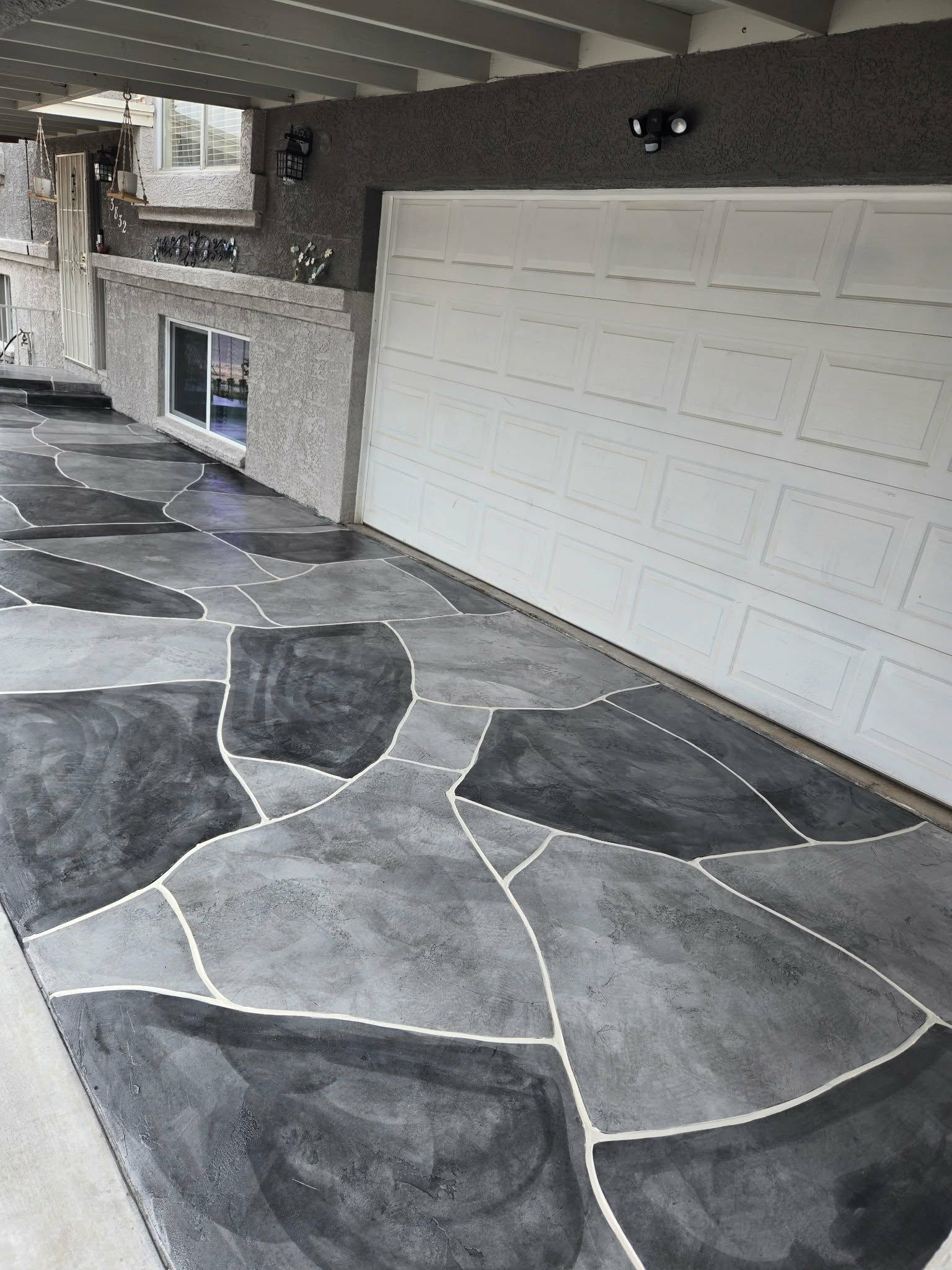 Covered patio with irregular gray stone floor, built-in grill, and white garage door.