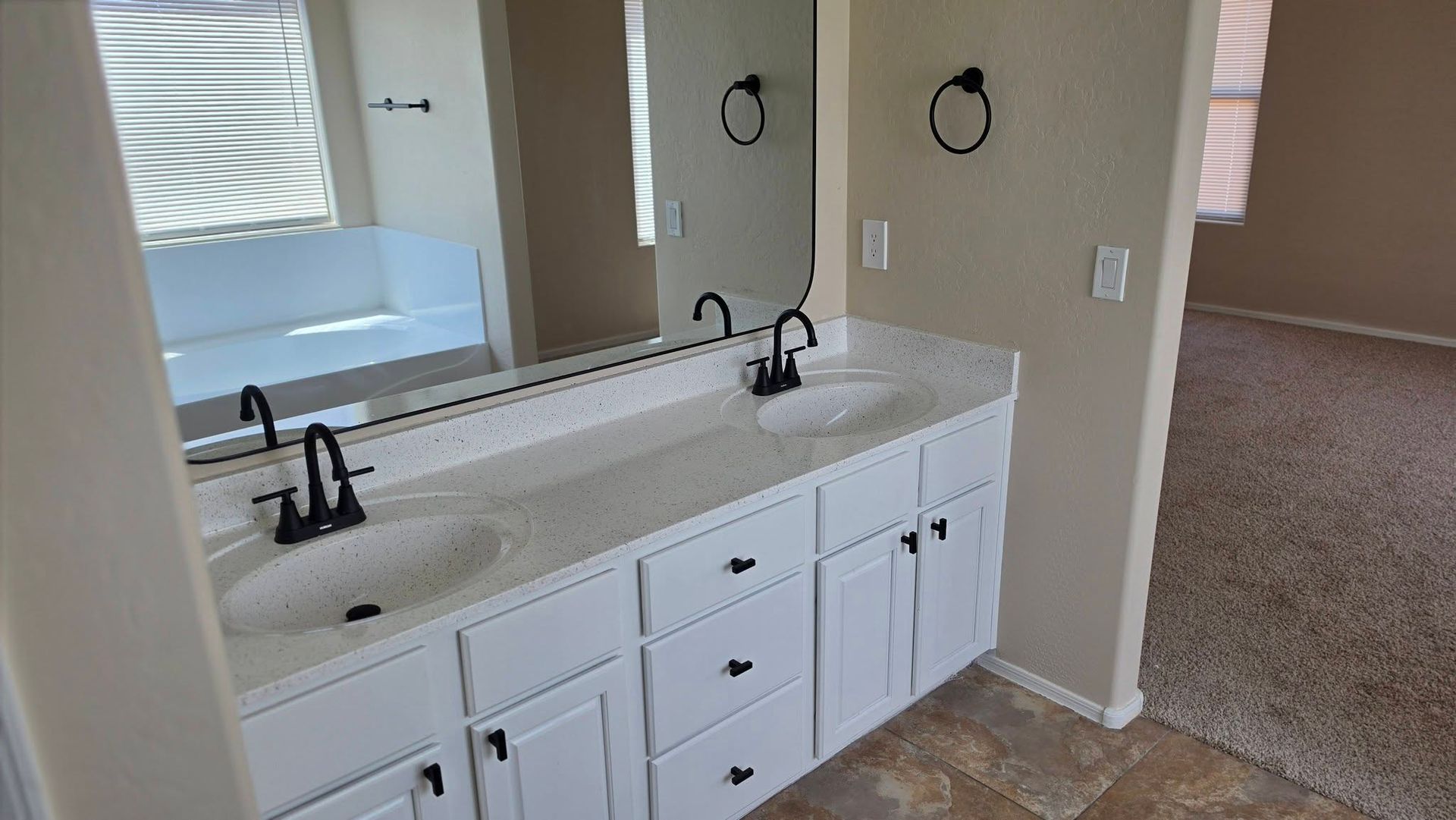 Bathroom vanity with double sinks, white cabinets, and two mirrors in a beige room