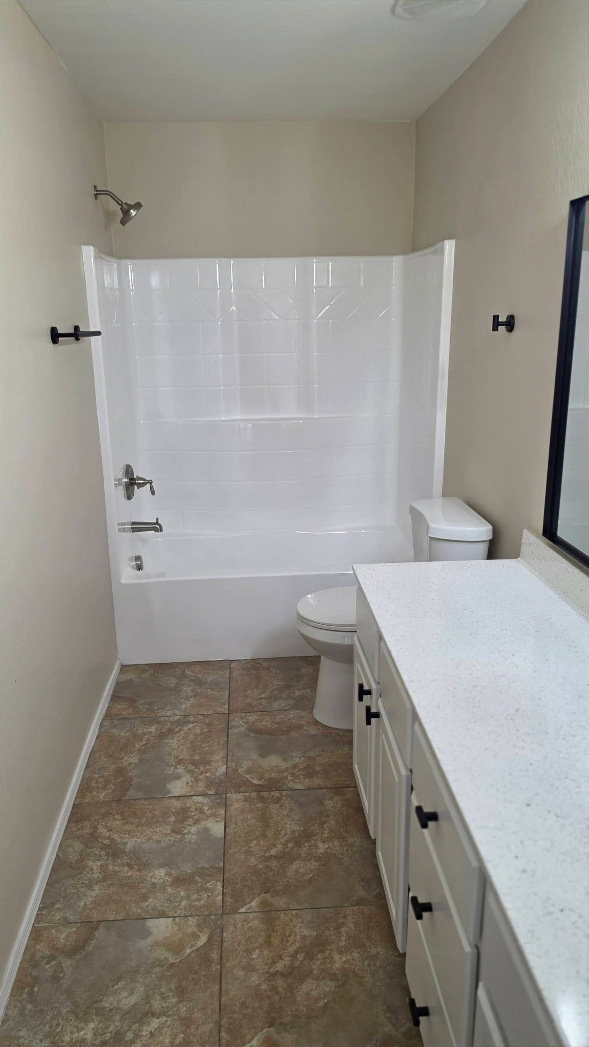 Small bathroom with a tub-shower, toilet, white vanity, and stone-pattern tile floor.