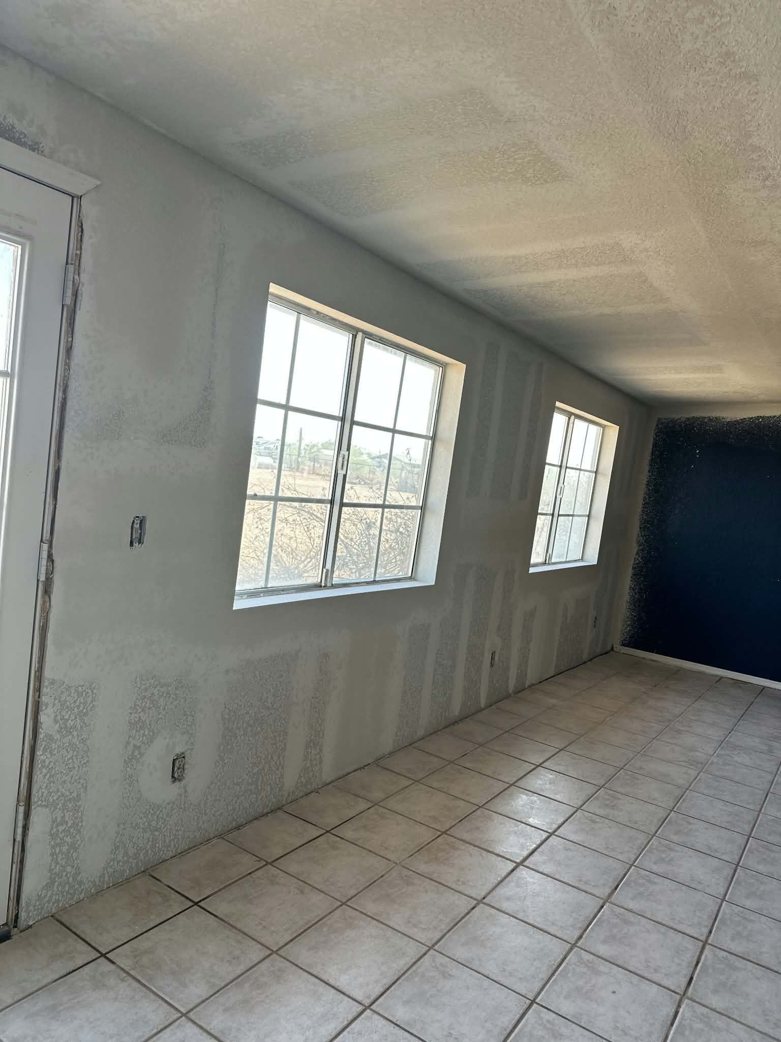Empty white room with tiled floor and two windows along one wall