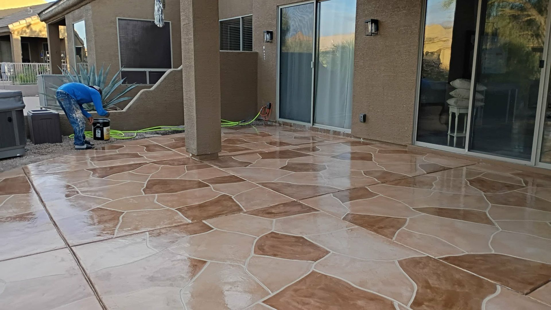 Worker power-washing a wet stone patio beside a modern building with glass doors