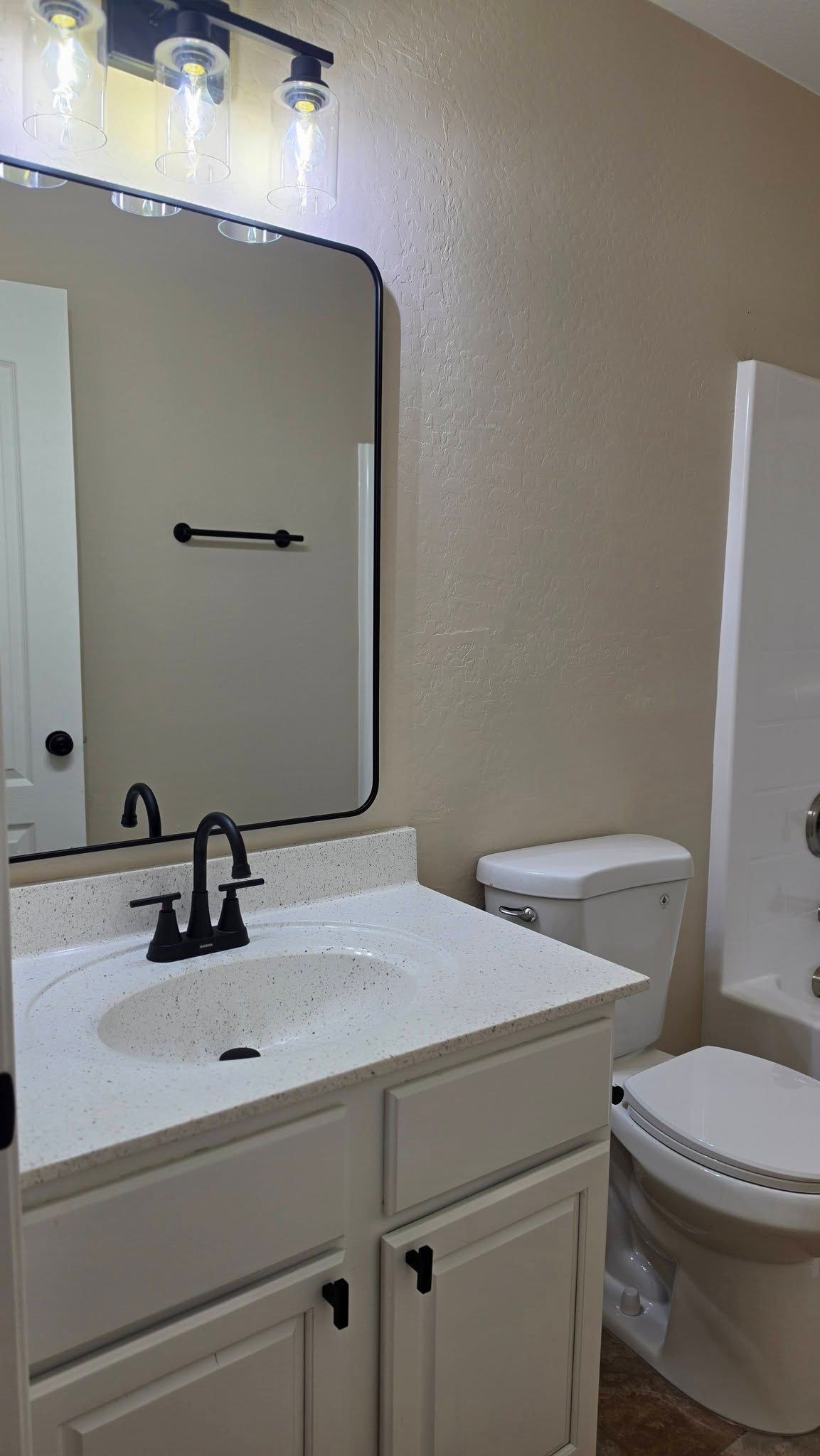 Small bathroom with white vanity, black faucet, mirror, toilet, and shower curtain.