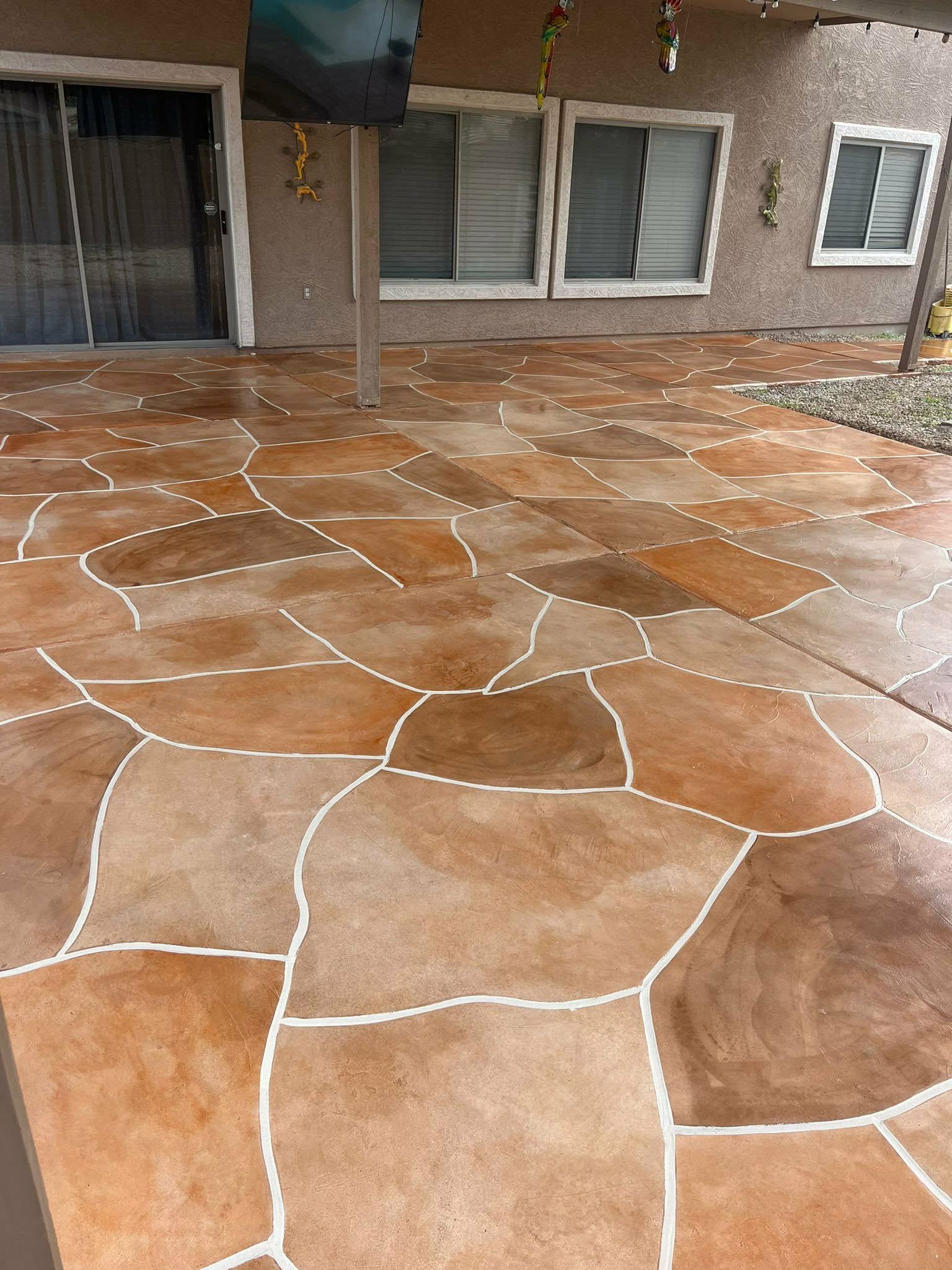 Stone-patterned patio with wet reddish-brown concrete in front of a building entrance and windows