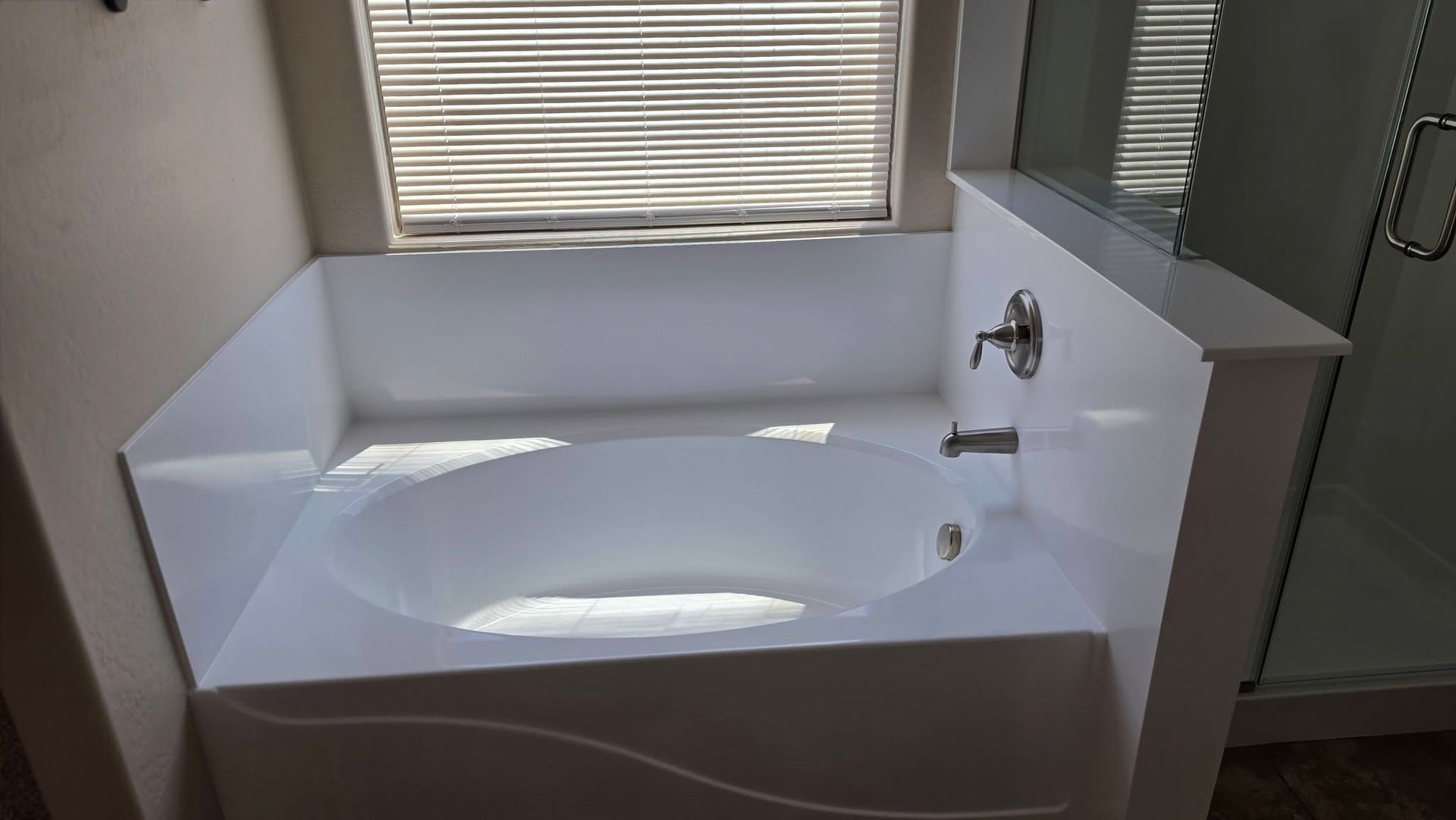 White freestanding bathtub with chrome faucet in a bright bathroom, lit by sunlight from a window.