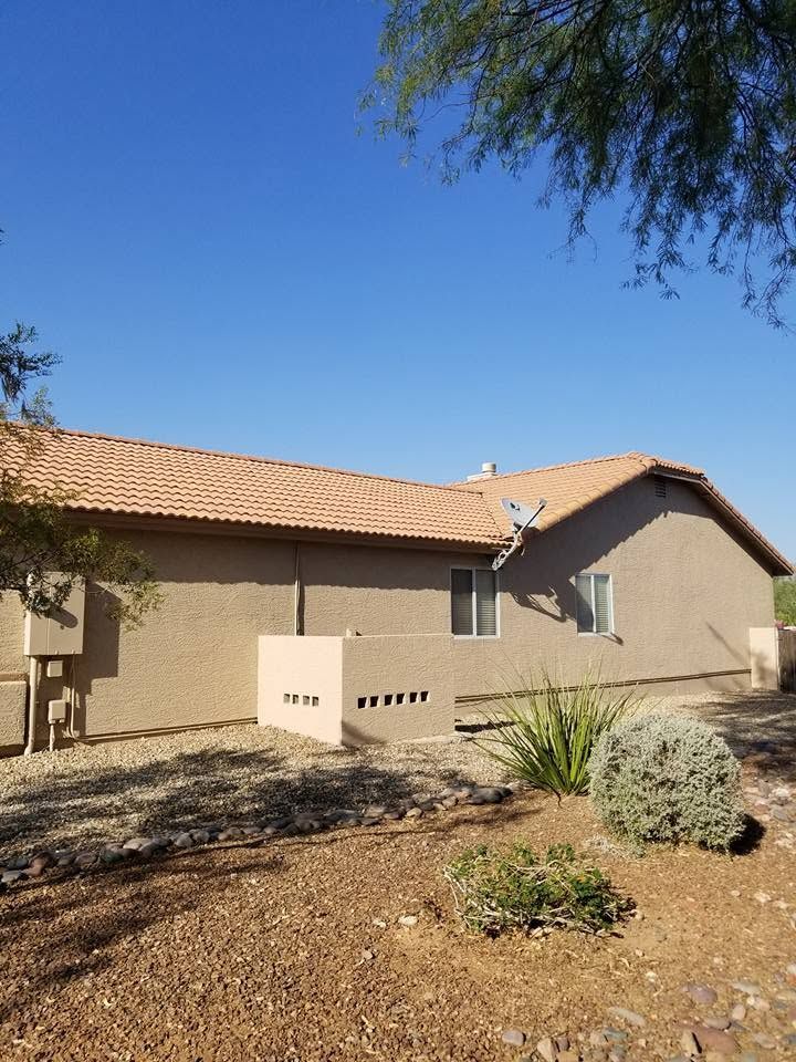 Single-story beige house with a tan tile roof in a dry desert yard under a clear blue sky