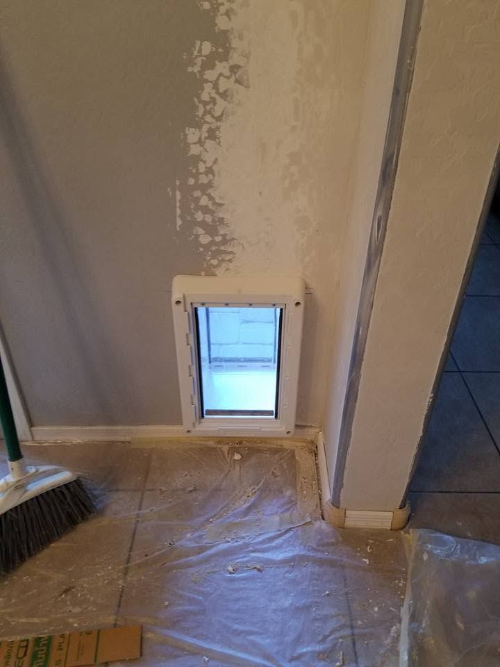 Small pet door in a wall, with a broom and covered floor in a room under renovation.