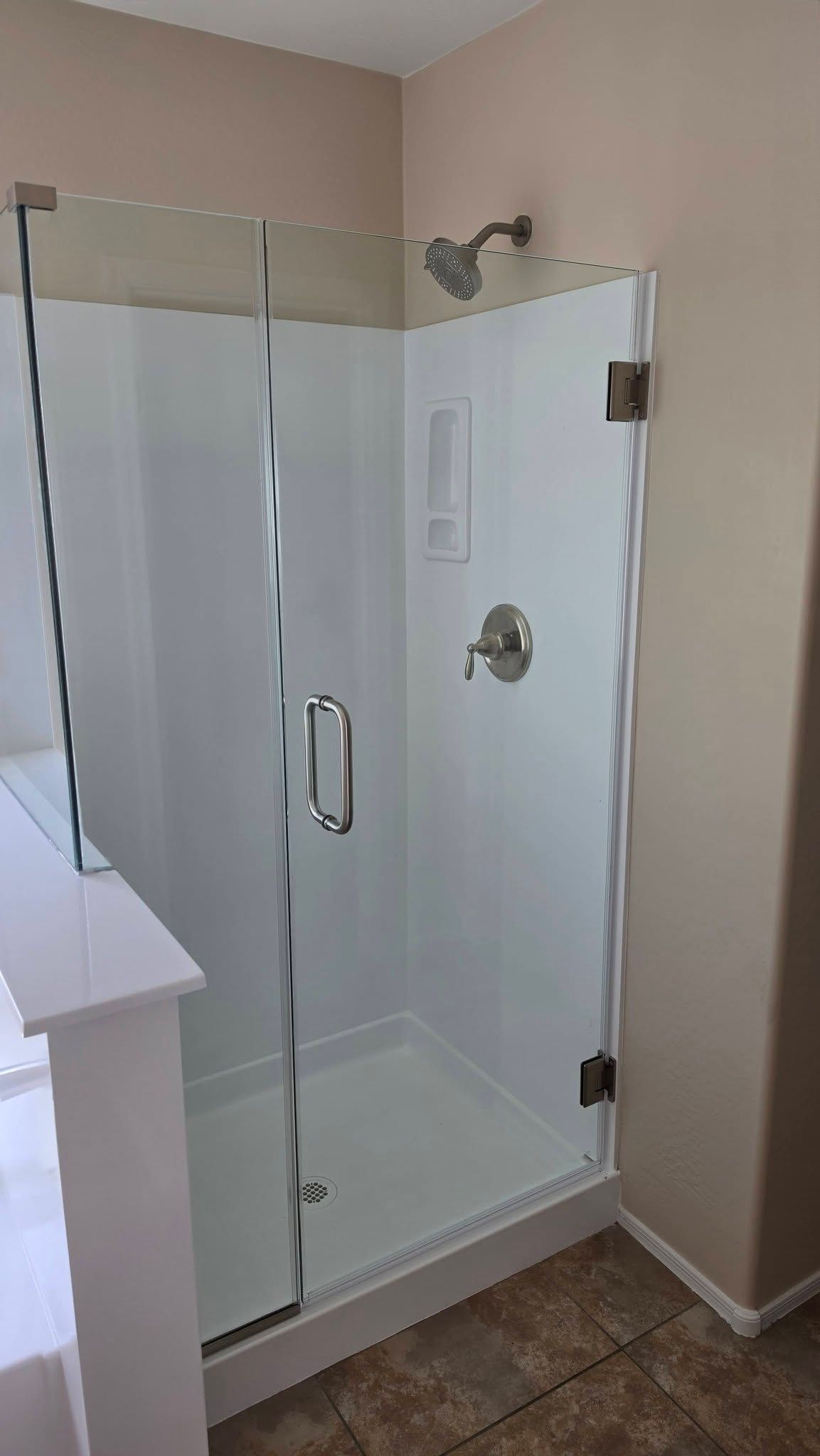White glass shower enclosure with chrome door in a beige bathroom
