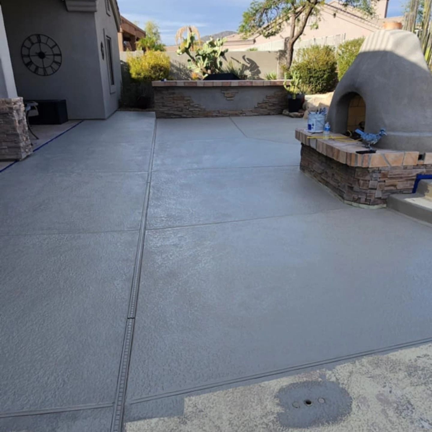 Empty concrete backyard patio with a built-in brick pizza oven and low retaining wall.