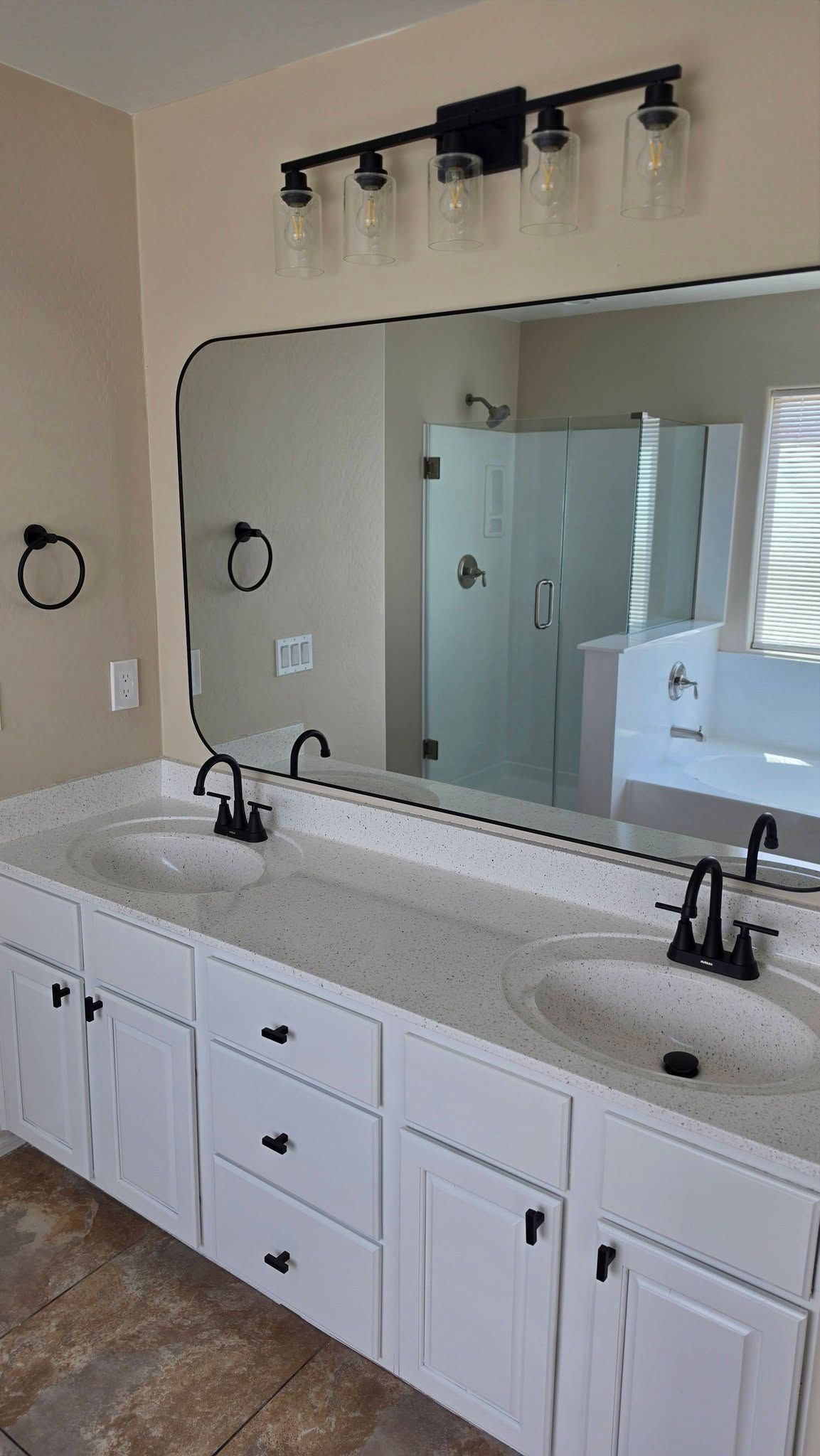 Bright bathroom vanity with double sinks, large mirror, wall sconces, and white cabinets