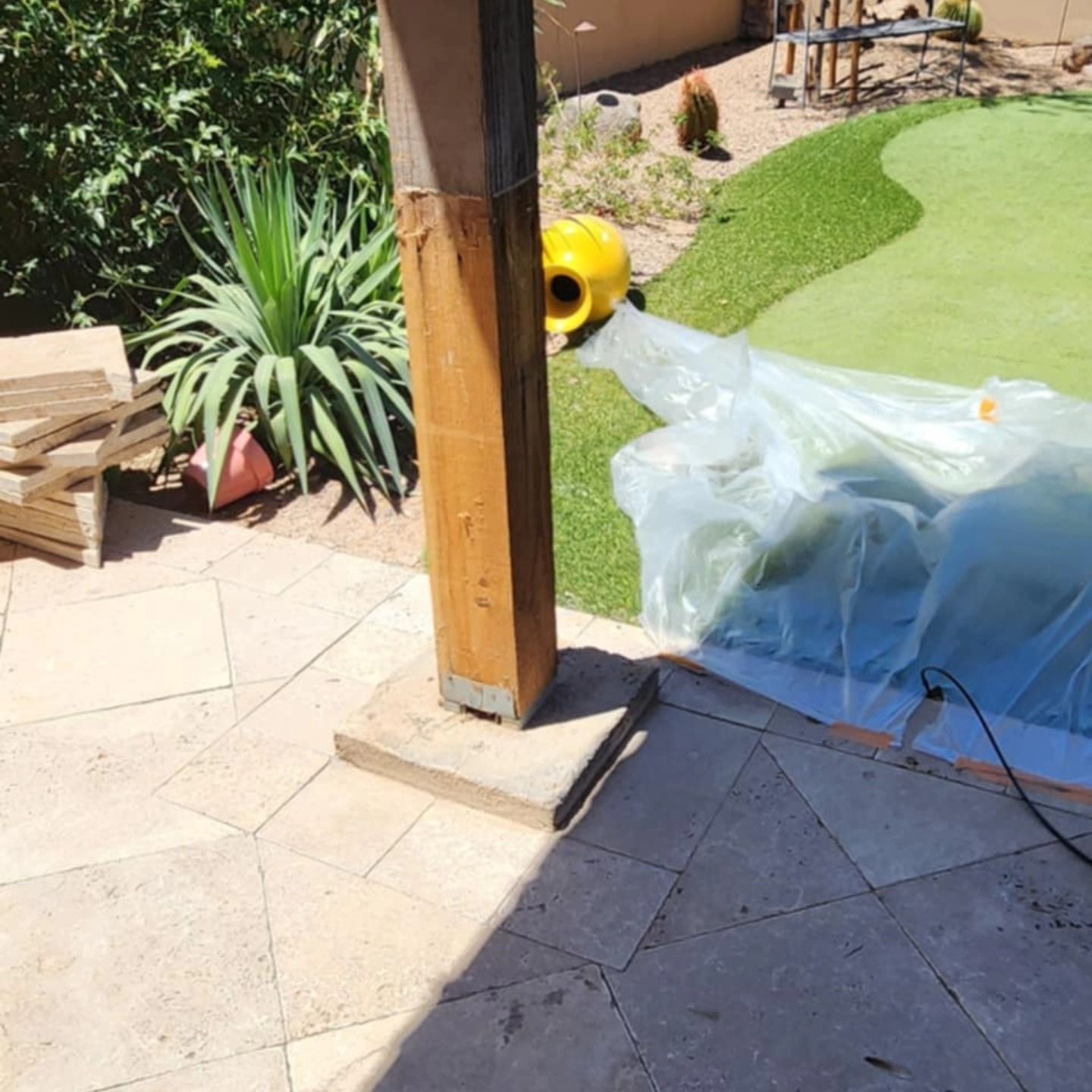 Patio with wooden post, potted plants, tarp-covered object, and green artificial grass in sunlight